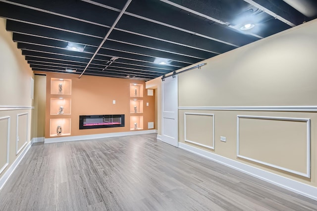 finished basement with a decorative wall, wood finished floors, built in features, a barn door, and a glass covered fireplace