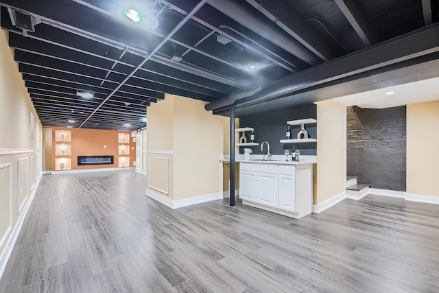 finished basement featuring bar area, baseboards, a large fireplace, a sink, and light wood-style floors