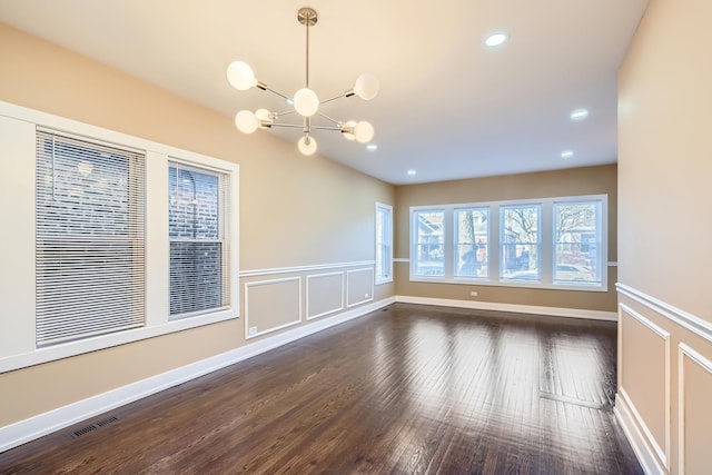 spare room with recessed lighting, dark wood finished floors, a decorative wall, a notable chandelier, and wainscoting