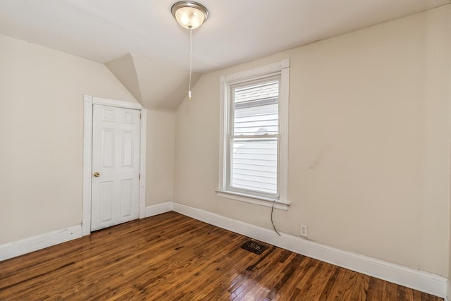 interior space featuring dark wood-type flooring, lofted ceiling, visible vents, and baseboards