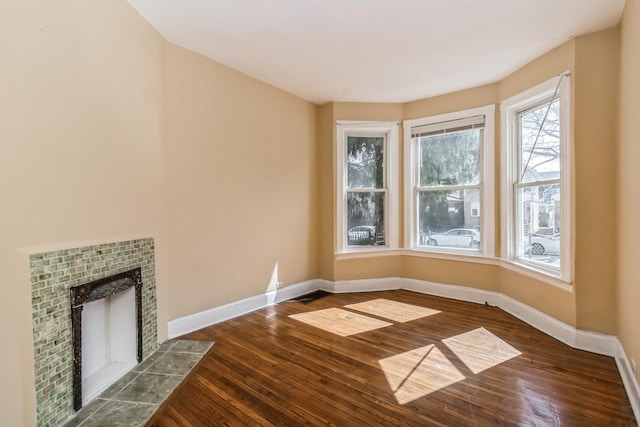 unfurnished living room with a tiled fireplace, baseboards, and wood finished floors