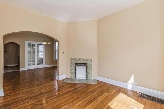 unfurnished living room with baseboards, visible vents, arched walkways, and wood-type flooring