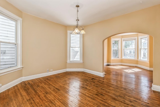 unfurnished room with arched walkways, baseboards, and hardwood / wood-style flooring