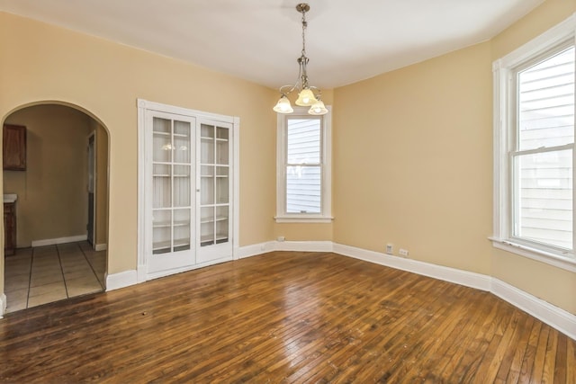 unfurnished room with plenty of natural light, a notable chandelier, arched walkways, and hardwood / wood-style floors
