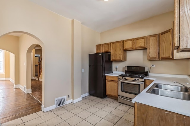 kitchen featuring light countertops, visible vents, stainless steel gas range, a sink, and freestanding refrigerator