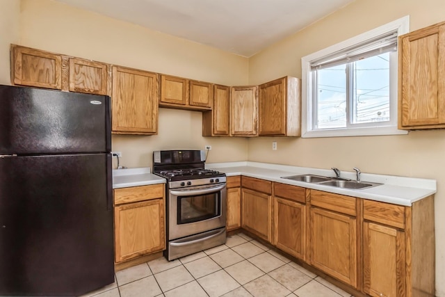 kitchen with light tile patterned flooring, light countertops, stainless steel range with gas stovetop, a sink, and freestanding refrigerator