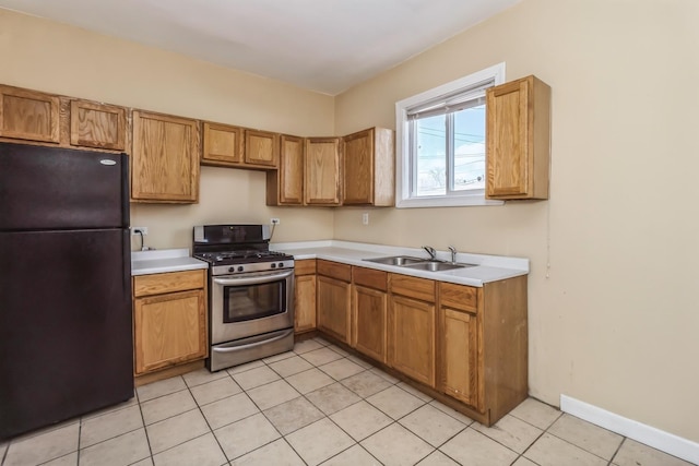 kitchen featuring stainless steel gas range oven, light countertops, light tile patterned floors, a sink, and freestanding refrigerator
