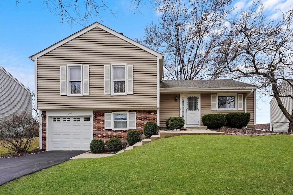 tri-level home with roof with shingles, driveway, a front yard, brick siding, and a garage