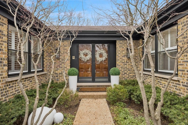doorway to property with brick siding and roof with shingles