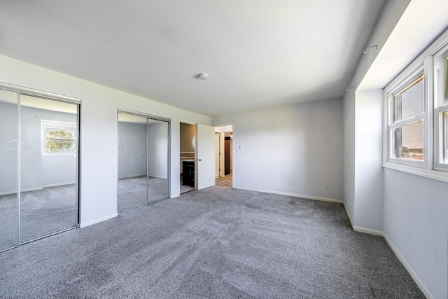 unfurnished bedroom with two closets, carpet flooring, and baseboards