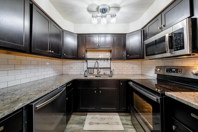 kitchen with decorative backsplash, light stone countertops, appliances with stainless steel finishes, a sink, and an inviting chandelier