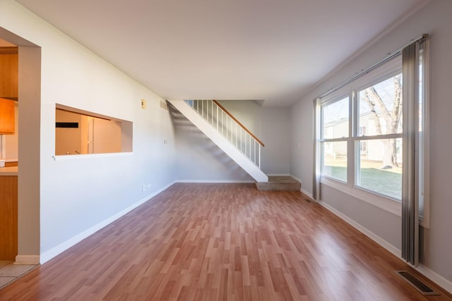unfurnished living room with stairway, baseboards, light wood finished floors, and visible vents