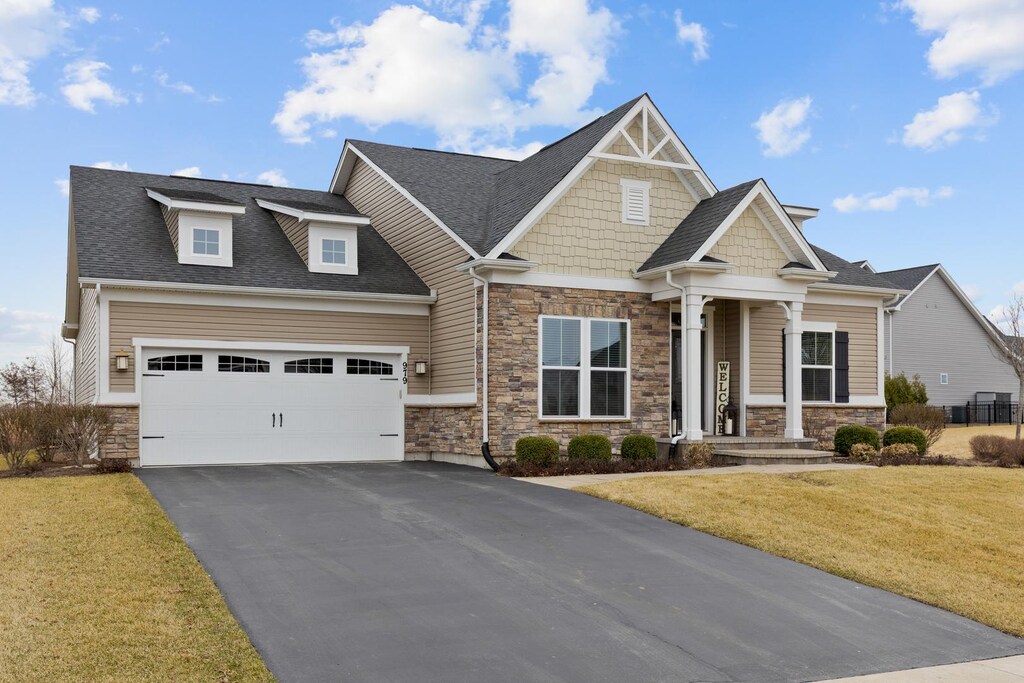 craftsman-style house featuring stone siding, a garage, aphalt driveway, and a front lawn