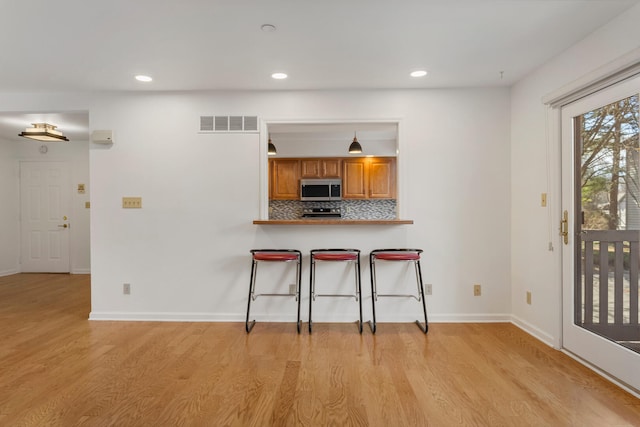 kitchen with light wood-type flooring, brown cabinetry, stainless steel microwave, visible vents, and decorative backsplash