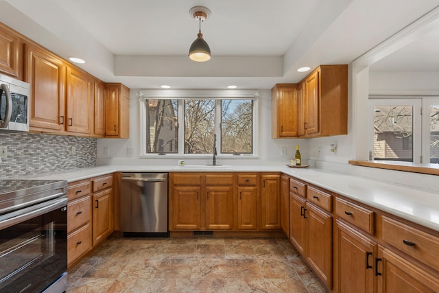 kitchen featuring light countertops, brown cabinets, appliances with stainless steel finishes, a sink, and backsplash