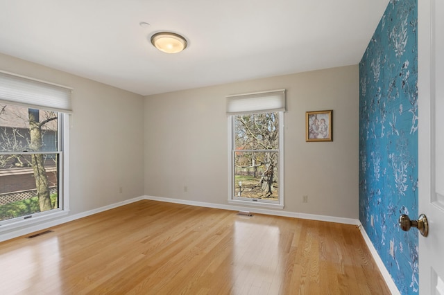 unfurnished room featuring baseboards, visible vents, light wood-style flooring, and a healthy amount of sunlight