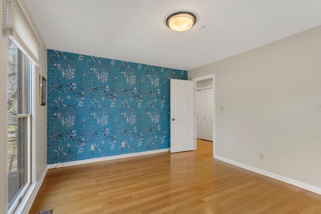 unfurnished room with baseboards, wallpapered walls, plenty of natural light, and wood finished floors