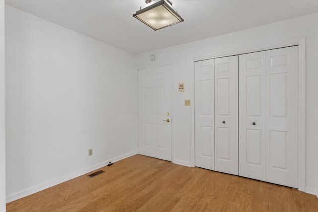 unfurnished bedroom featuring baseboards, light wood-type flooring, visible vents, and a closet