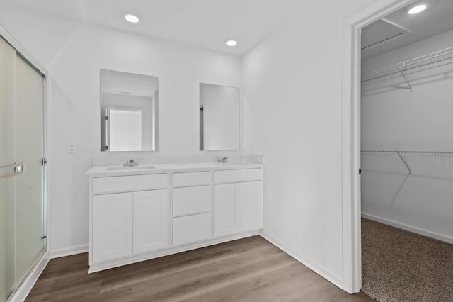 full bath featuring a spacious closet, double vanity, a sink, and wood finished floors