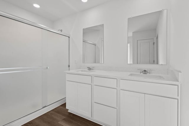 bathroom with a shower stall, double vanity, wood finished floors, and a sink