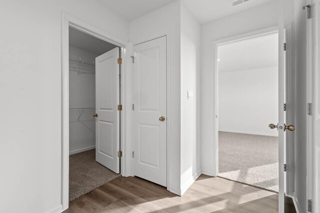 corridor with baseboards, visible vents, and wood finished floors