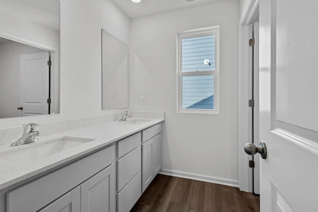 full bath featuring baseboards, wood finished floors, double vanity, and a sink
