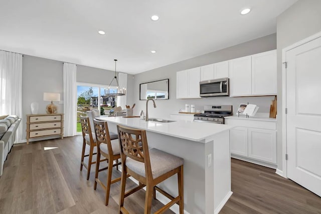 kitchen featuring light countertops, a sink, a kitchen breakfast bar, appliances with stainless steel finishes, and dark wood finished floors