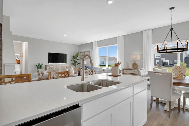 kitchen with a notable chandelier, a sink, stainless steel dishwasher, open floor plan, and white cabinets