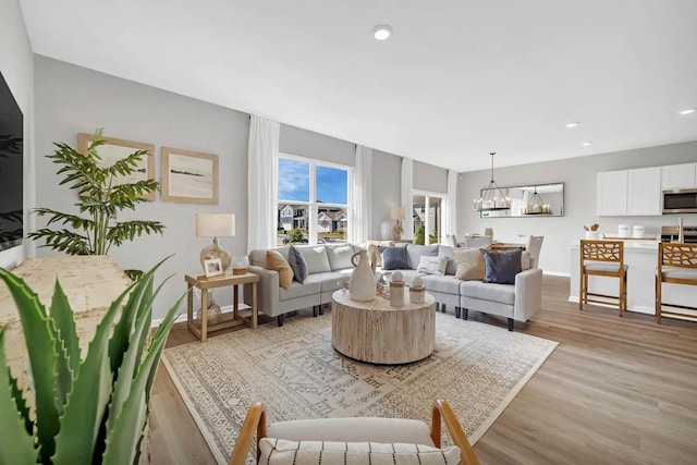 living area featuring baseboards, a notable chandelier, light wood-style flooring, and recessed lighting