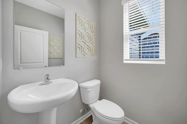 half bath featuring toilet, a sink, baseboards, and a wealth of natural light