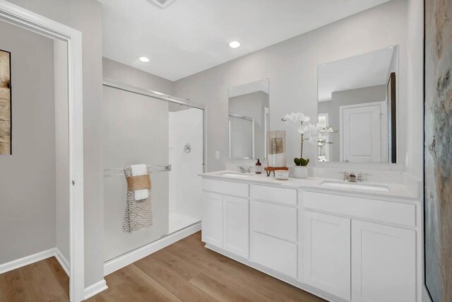 bathroom featuring a stall shower, double vanity, wood finished floors, and a sink