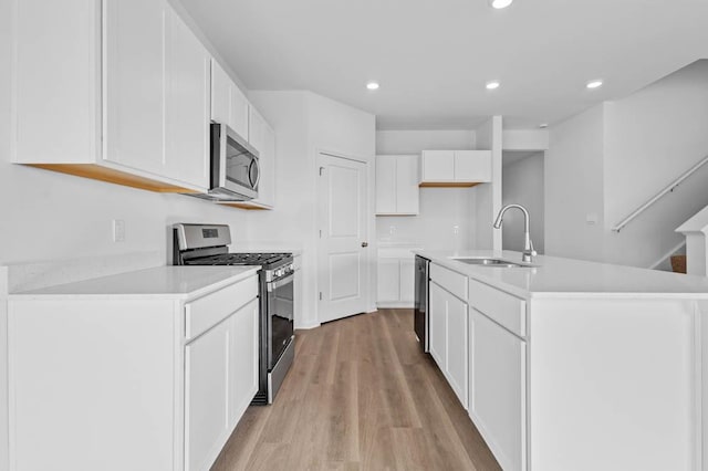 kitchen with light countertops, a sink, appliances with stainless steel finishes, light wood-type flooring, and white cabinets