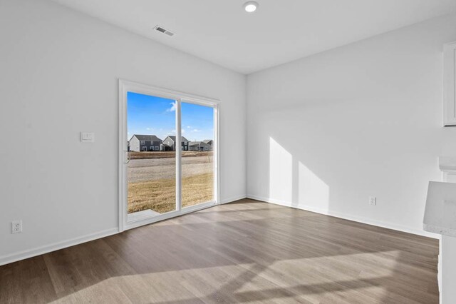 empty room featuring wood finished floors, baseboards, and visible vents