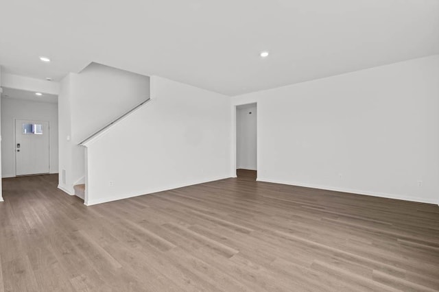 unfurnished living room with stairs, recessed lighting, wood finished floors, and baseboards
