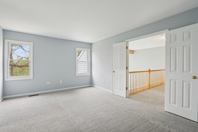 spare room with a healthy amount of sunlight, carpet floors, baseboards, and visible vents