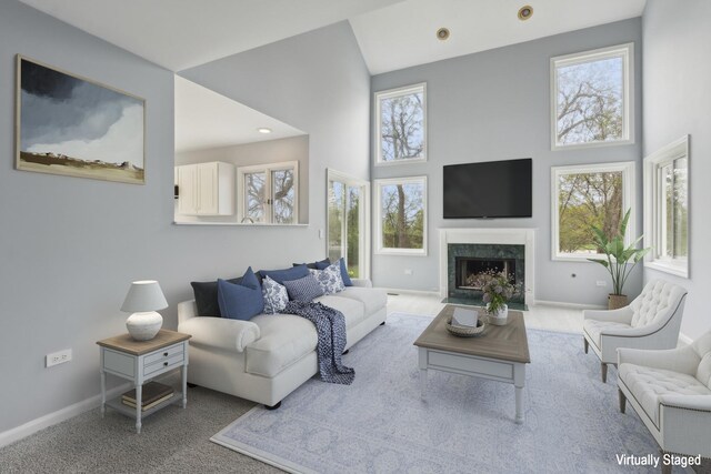 carpeted living room featuring baseboards, plenty of natural light, a high ceiling, and a fireplace