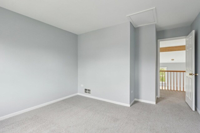 empty room featuring baseboards, visible vents, attic access, and light colored carpet