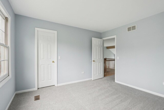 unfurnished bedroom featuring carpet floors, multiple windows, and visible vents