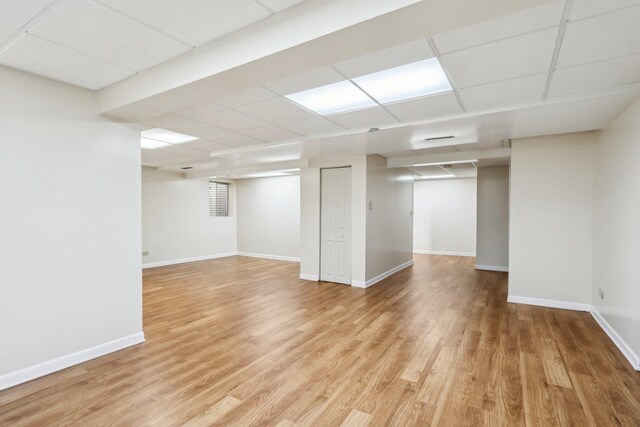 finished below grade area with light wood-style floors, baseboards, and a paneled ceiling