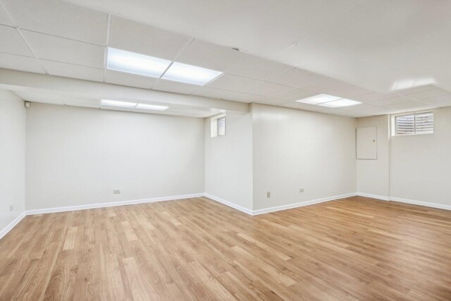 below grade area featuring light wood-type flooring, baseboards, and a drop ceiling