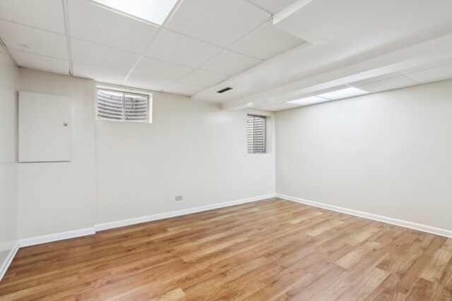 finished basement with baseboards, light wood-style floors, a drop ceiling, and visible vents