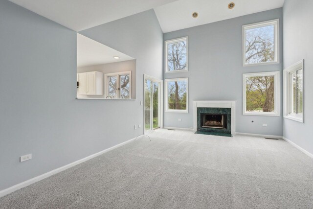 unfurnished living room with baseboards, a high ceiling, light carpet, and a premium fireplace
