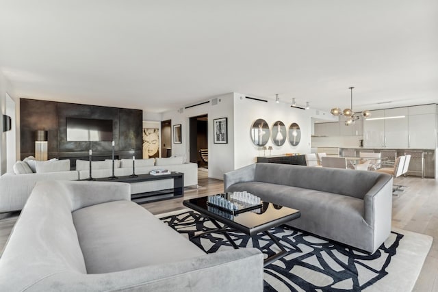 living room with a notable chandelier, track lighting, and light wood-type flooring