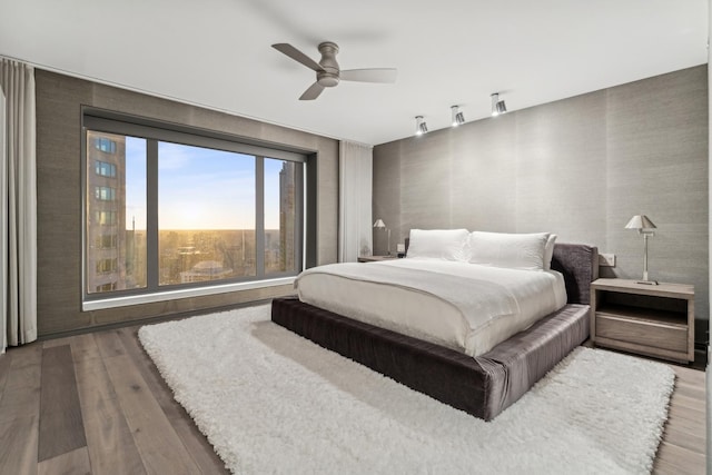 bedroom with wallpapered walls, wood finished floors, and a ceiling fan