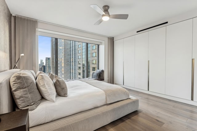 bedroom with ceiling fan, light wood-style flooring, and a view of city
