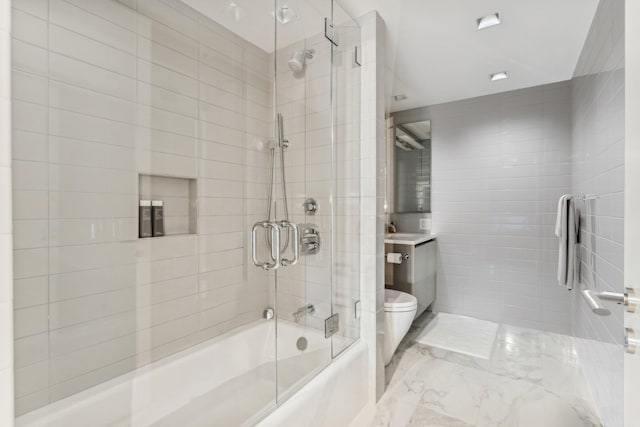 bathroom featuring tile walls, marble finish floor, toilet, vanity, and shower / bath combination with glass door