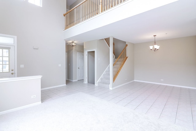 unfurnished living room featuring a towering ceiling, light tile patterned floors, baseboards, stairway, and an inviting chandelier