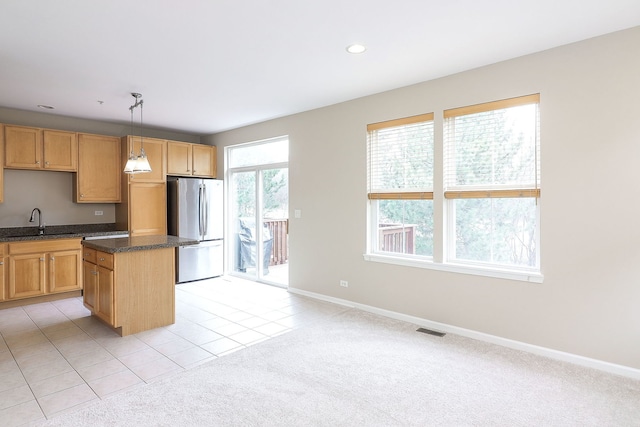 kitchen featuring visible vents, a center island, a sink, baseboards, and freestanding refrigerator