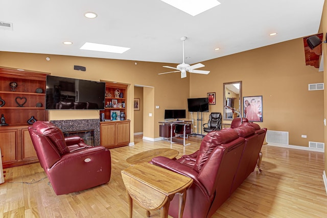living room with light wood finished floors, visible vents, lofted ceiling with skylight, and a glass covered fireplace