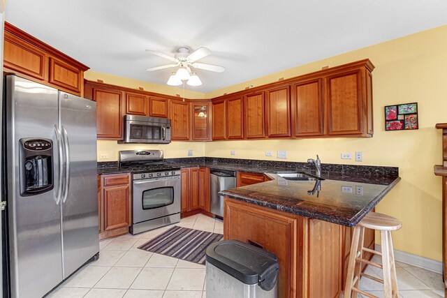 kitchen with light tile patterned flooring, a peninsula, a ceiling fan, appliances with stainless steel finishes, and a sink